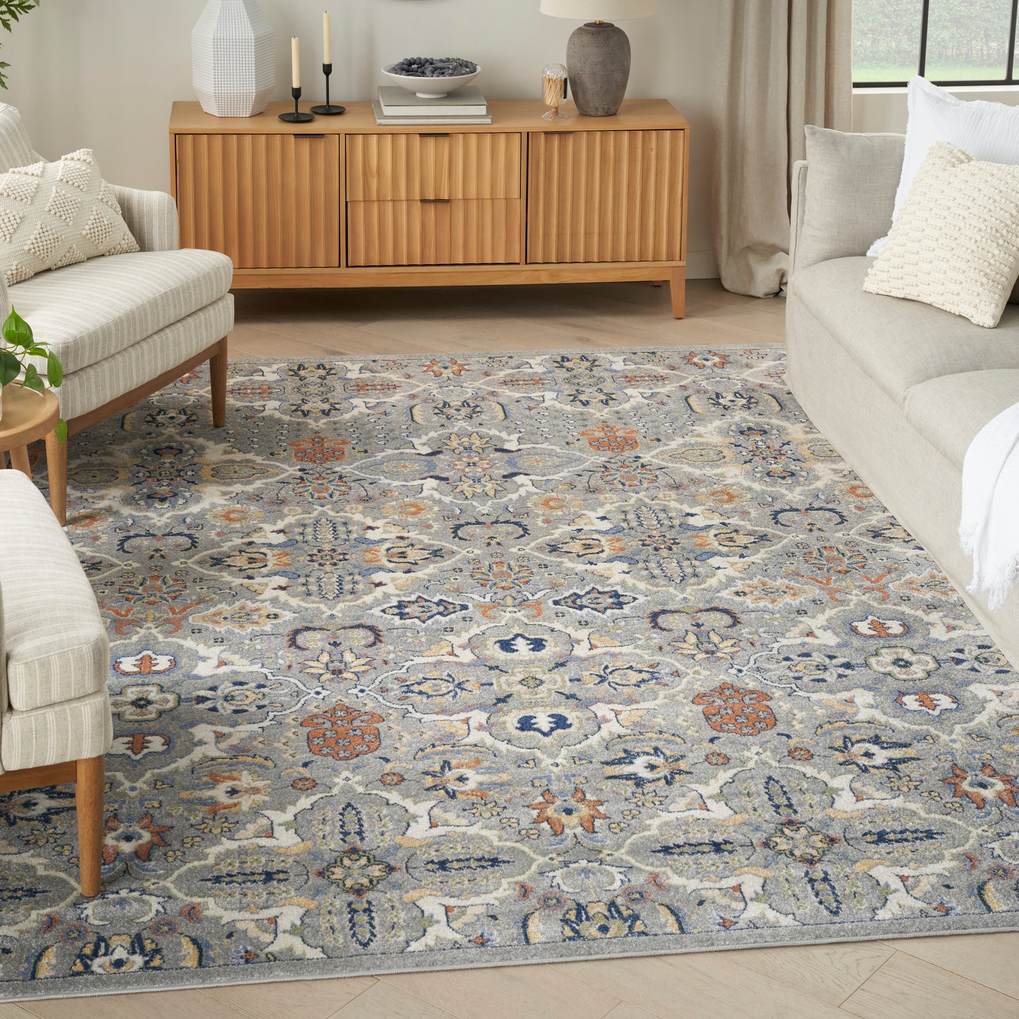 Rectangular blue gray Persian-style woven rug with ivory, orange and navy motifs under beige seating and wood sideboard.