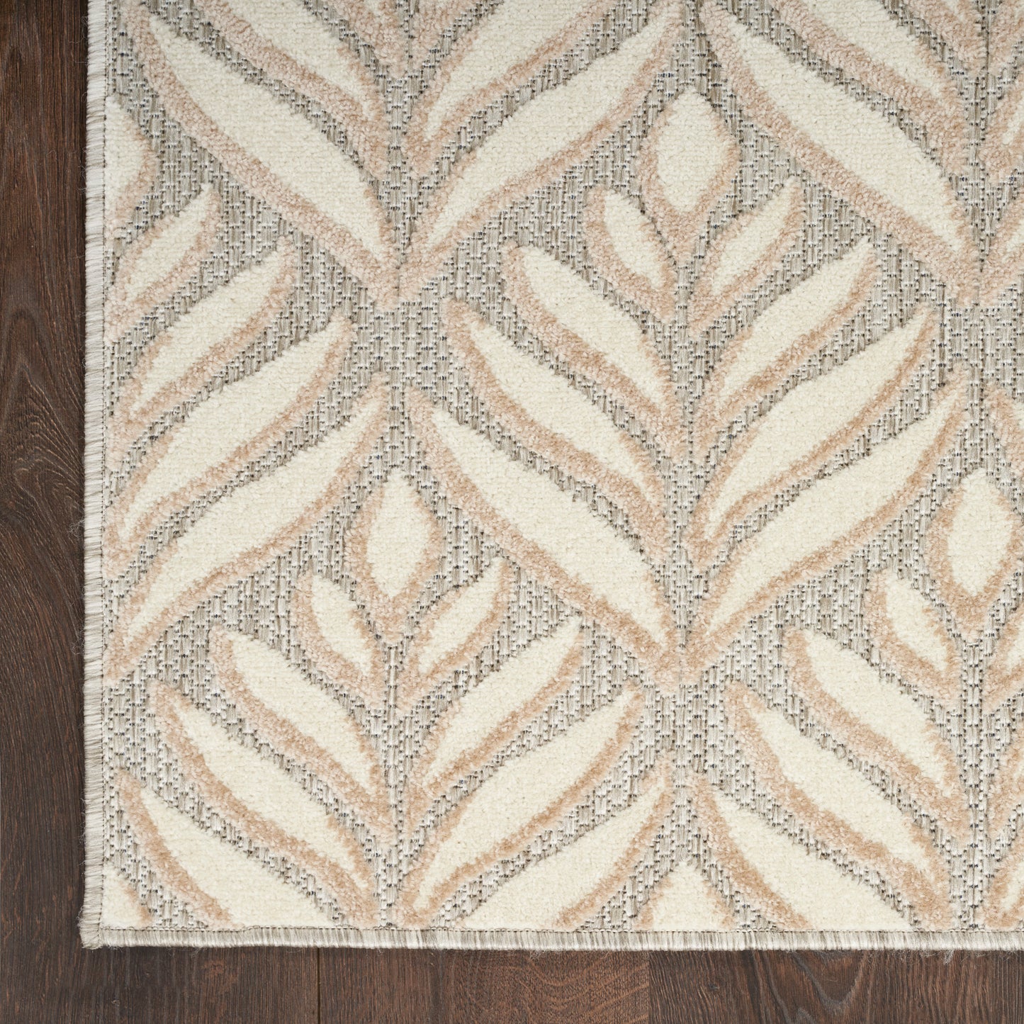 Beige and cream leaf-pattern area rug with gray woven background and fringed edges on wood floor.