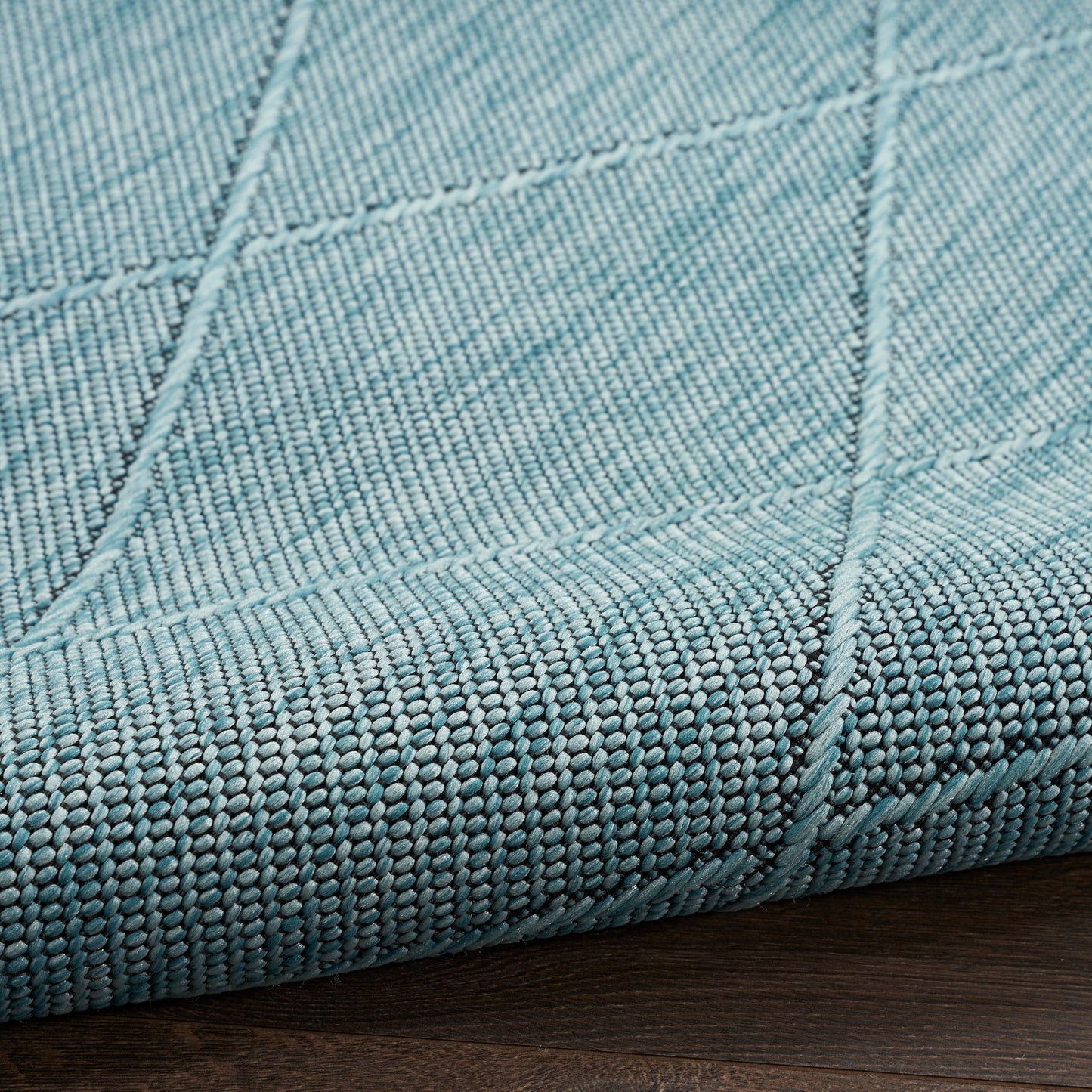 Teal woven rug with visible panel seams and a thick edge on a dark wood floor.