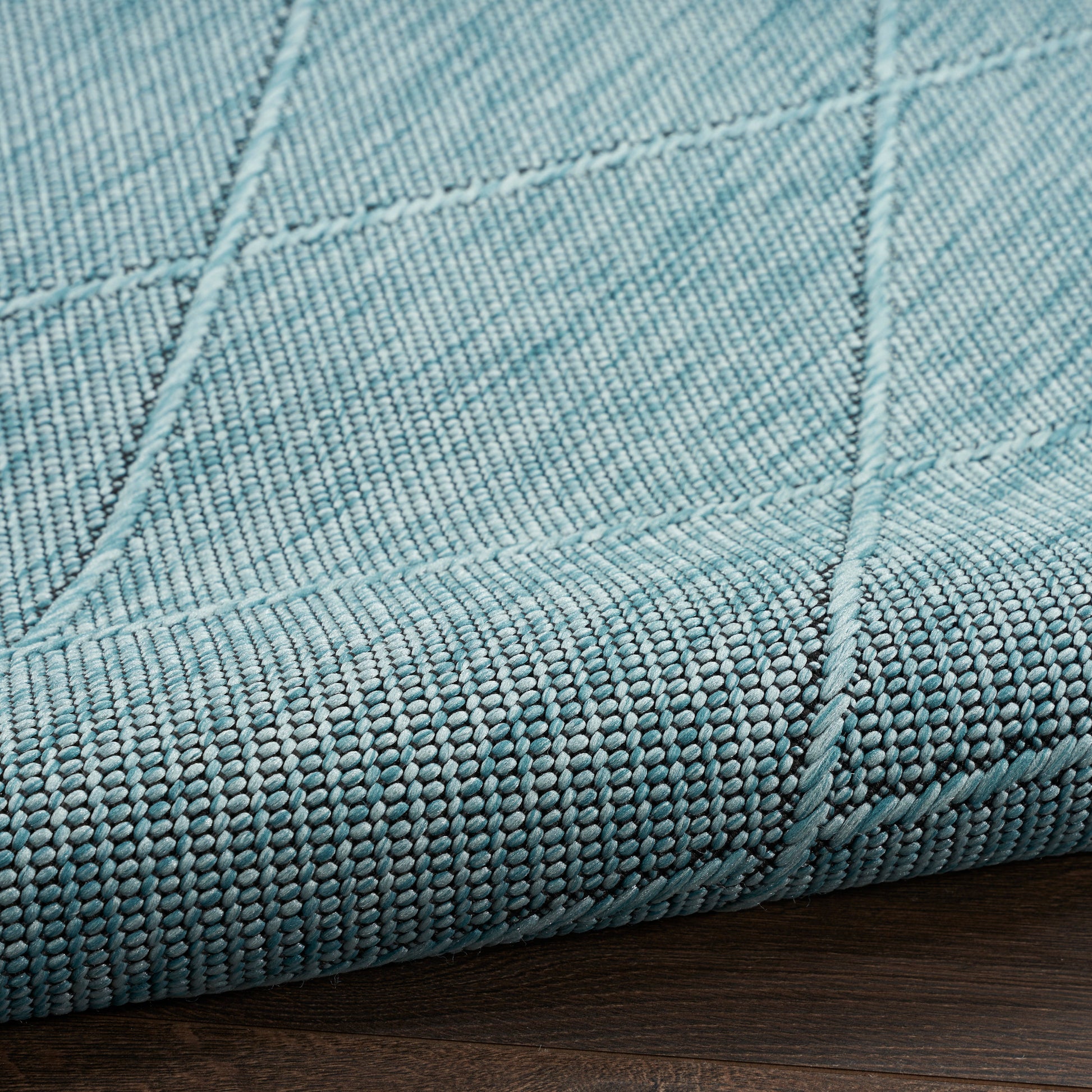 Teal woven rug with visible panel seams and a thick edge on a dark wood floor.