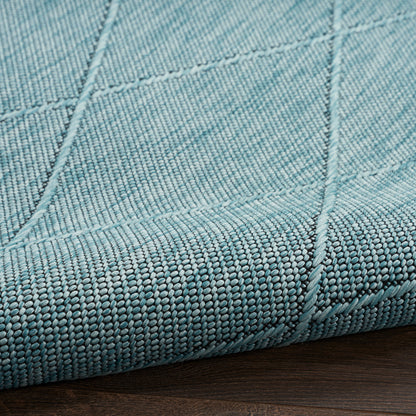 Teal woven rug with visible panel seams and a thick edge on a dark wood floor.