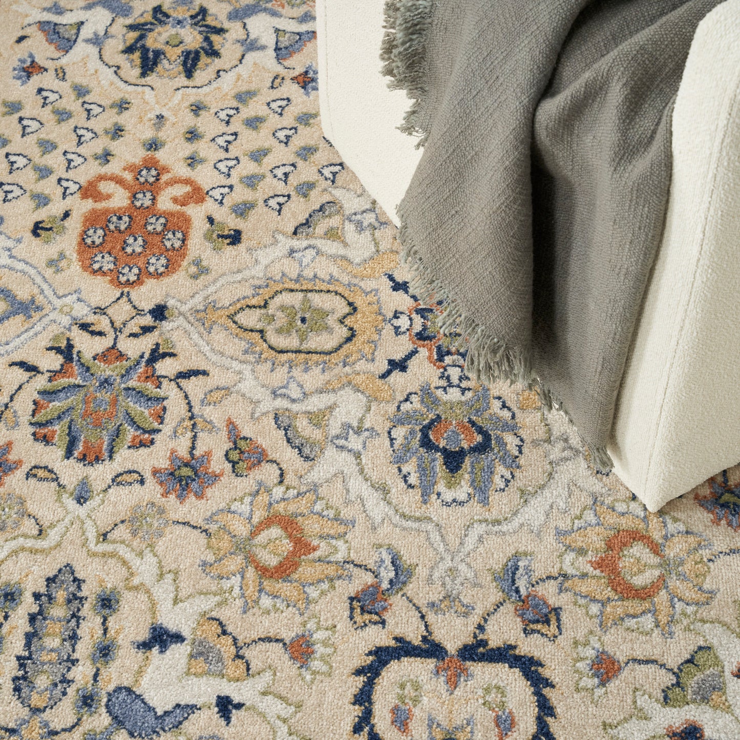Beige oriental-style rug with blue, orange, and green floral medallions; gray fringed throw over cream furniture.