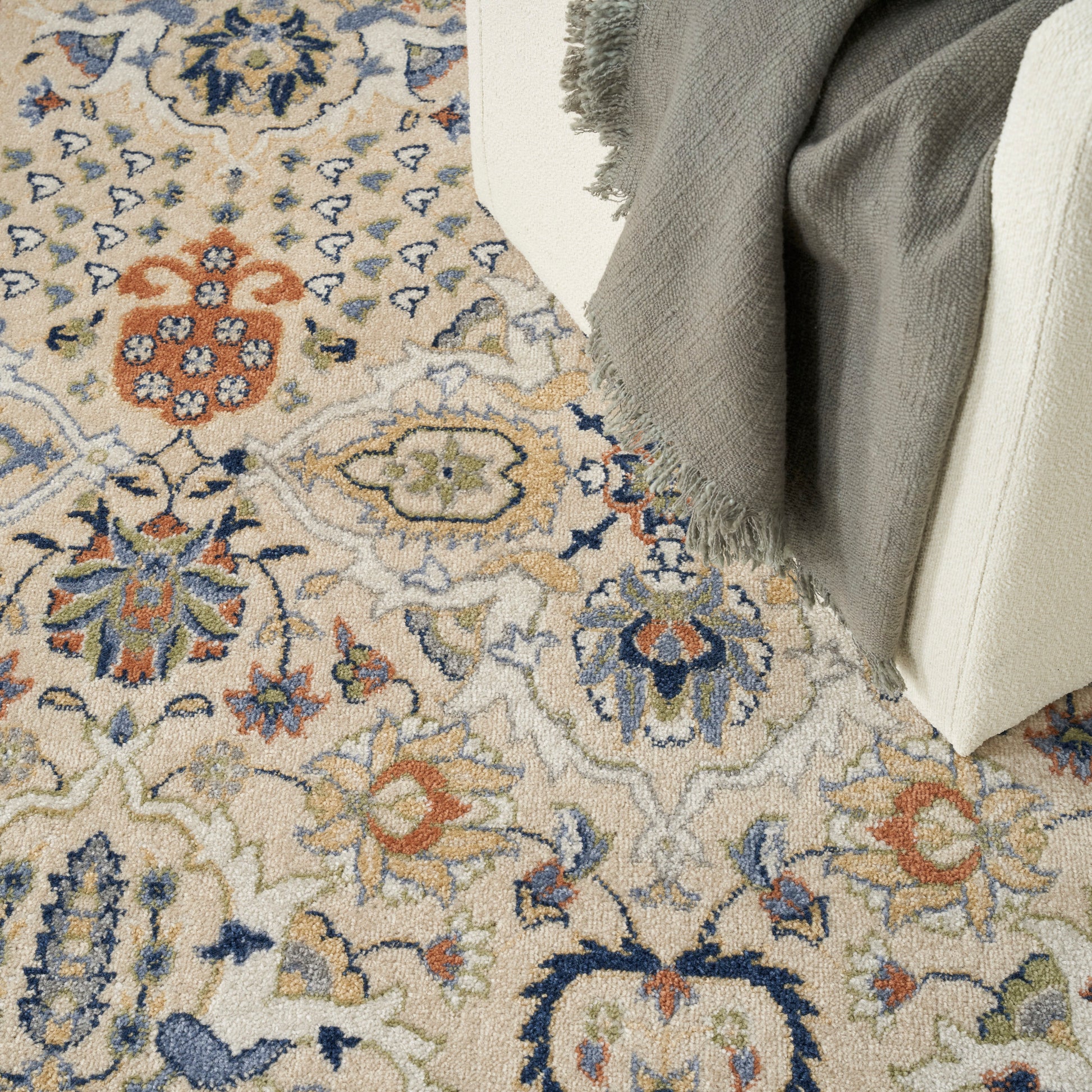 Beige oriental-style rug with blue, orange, and green floral medallions; gray fringed throw over cream furniture.