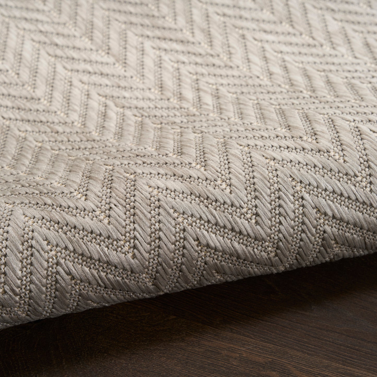 Beige woven rug with chevron pattern, thick textured fabric on dark wood floor.