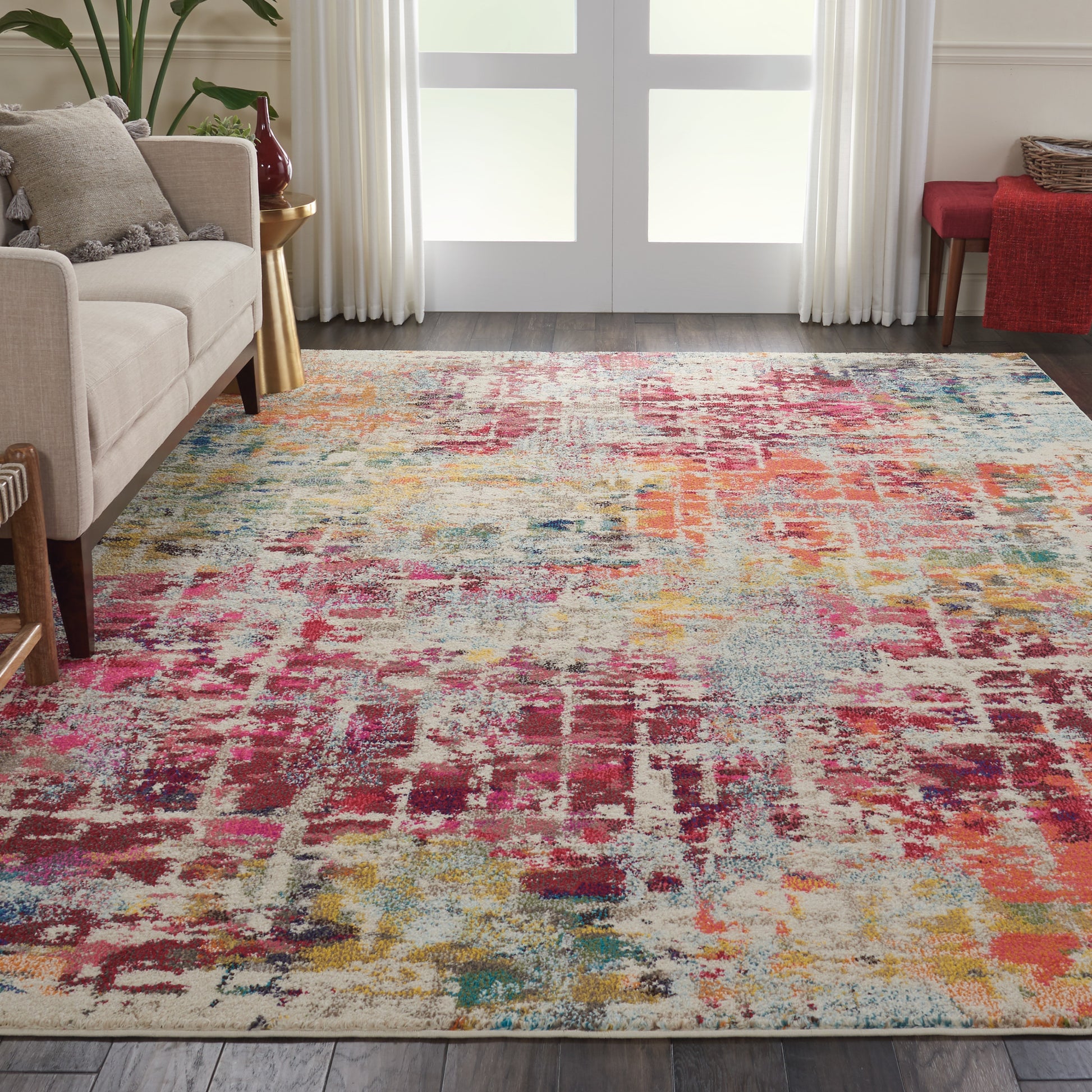 Abstract multicolor area rug with pink, yellow, blue and red tones in a living room with beige sofa and glass doors.
