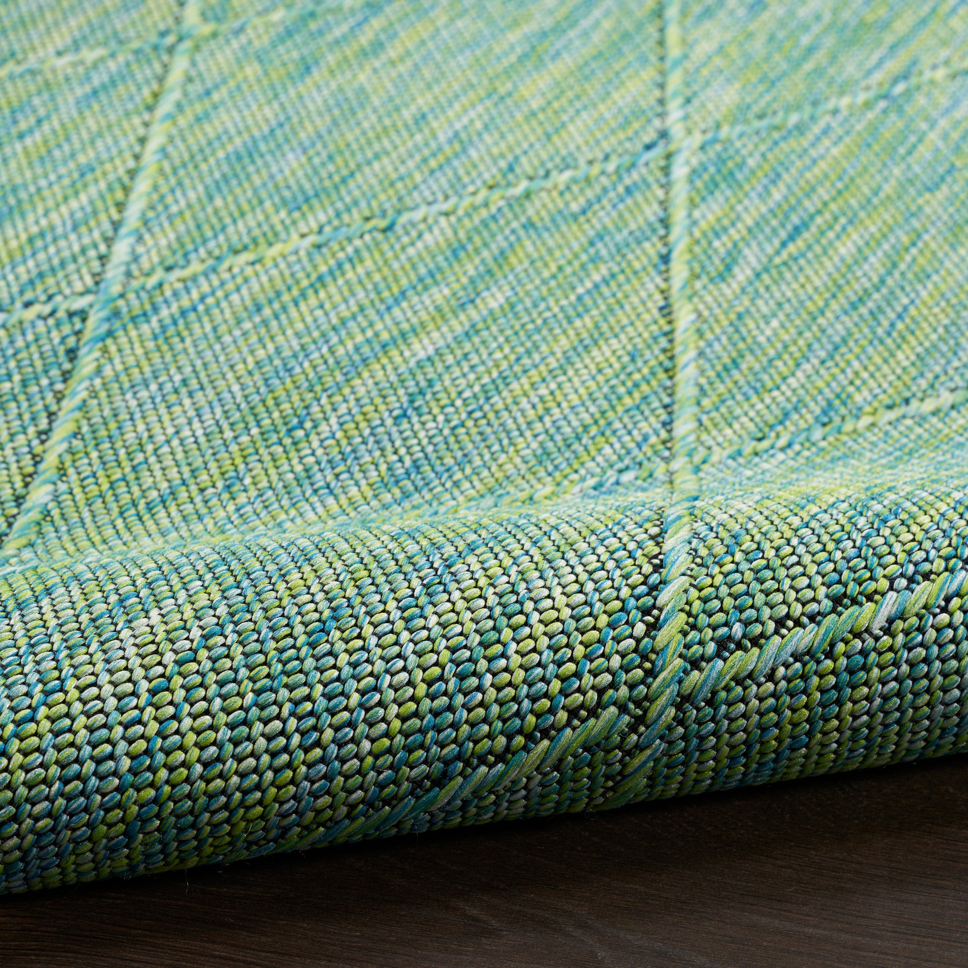 Close-up of green & blue woven rug with tight yarn texture and stitched square panel seams.