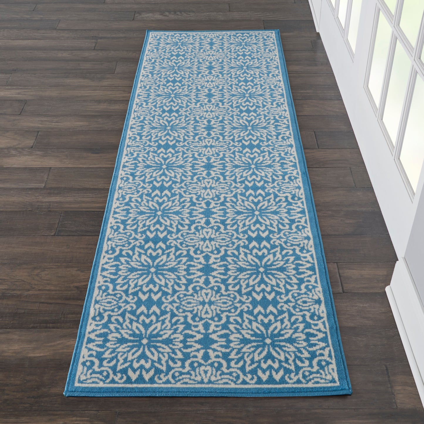 Narrow blue & beige damask-pattern runner rug with teal border on dark wood floor, 7' long.