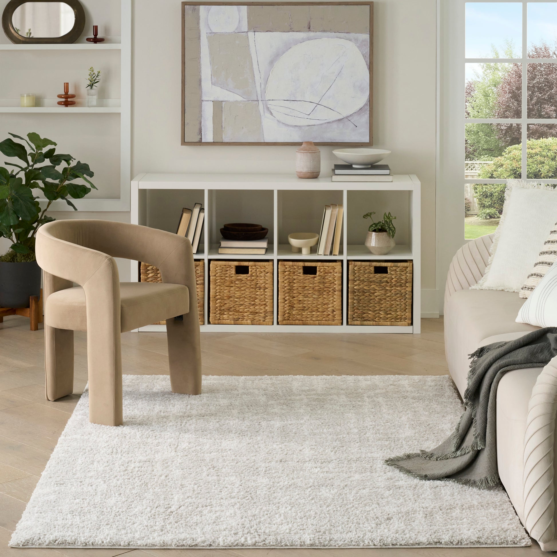 Beige sculptural curved lounge chair in a bright neutral living room with a white storage shelf and abstract art.