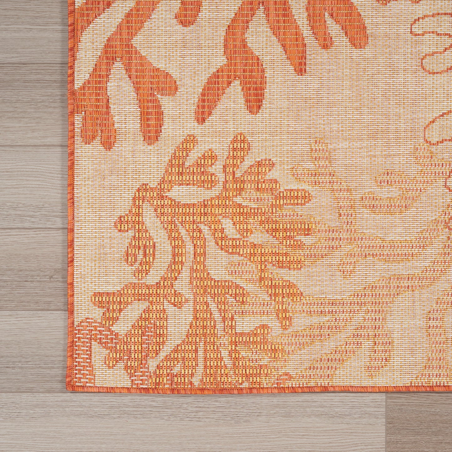 Rectangular woven area rug in orange and peach botanical pattern on cream background with orange border on wood floor.