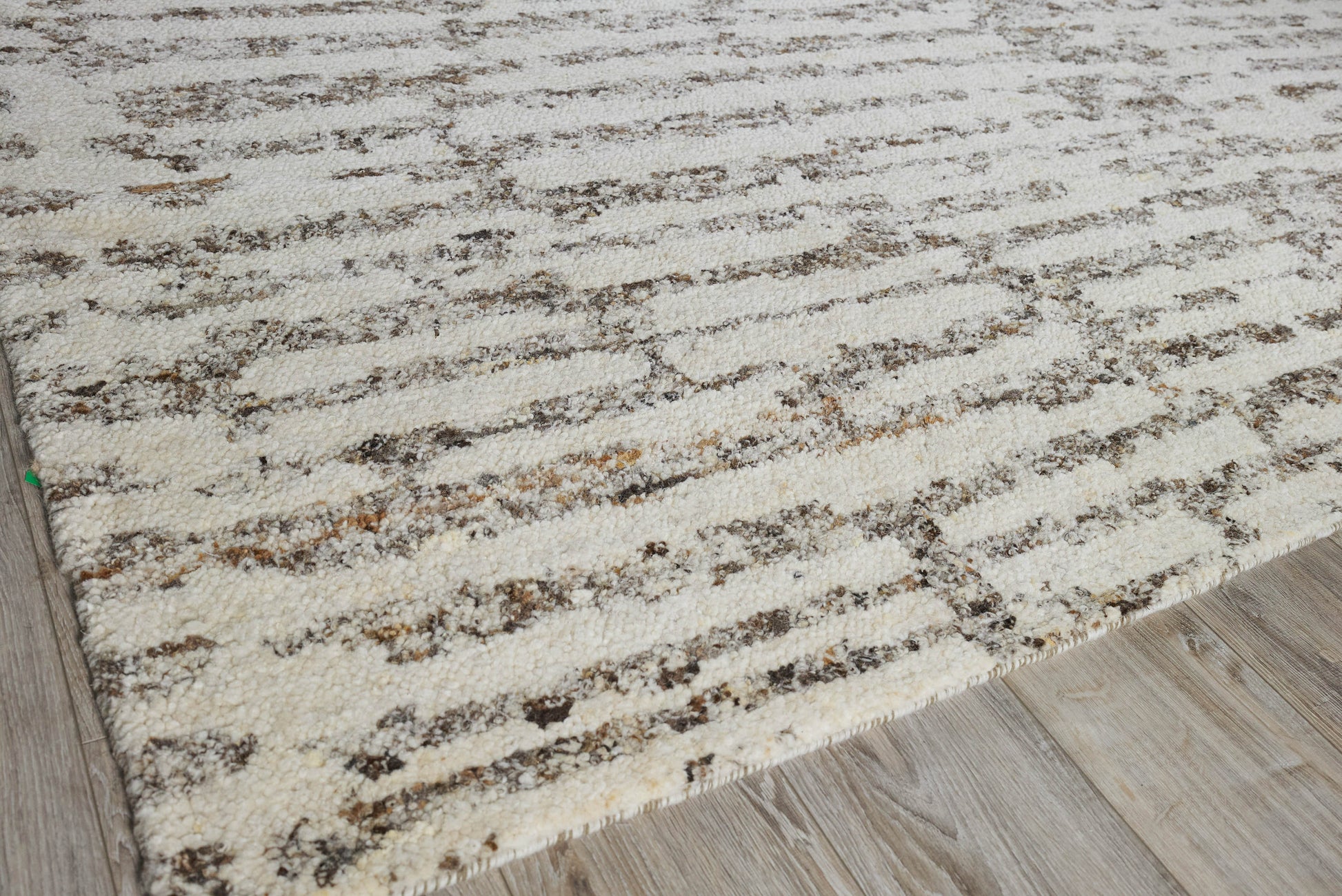 Beige cream area rug with brown irregular stripes on light wood floor.