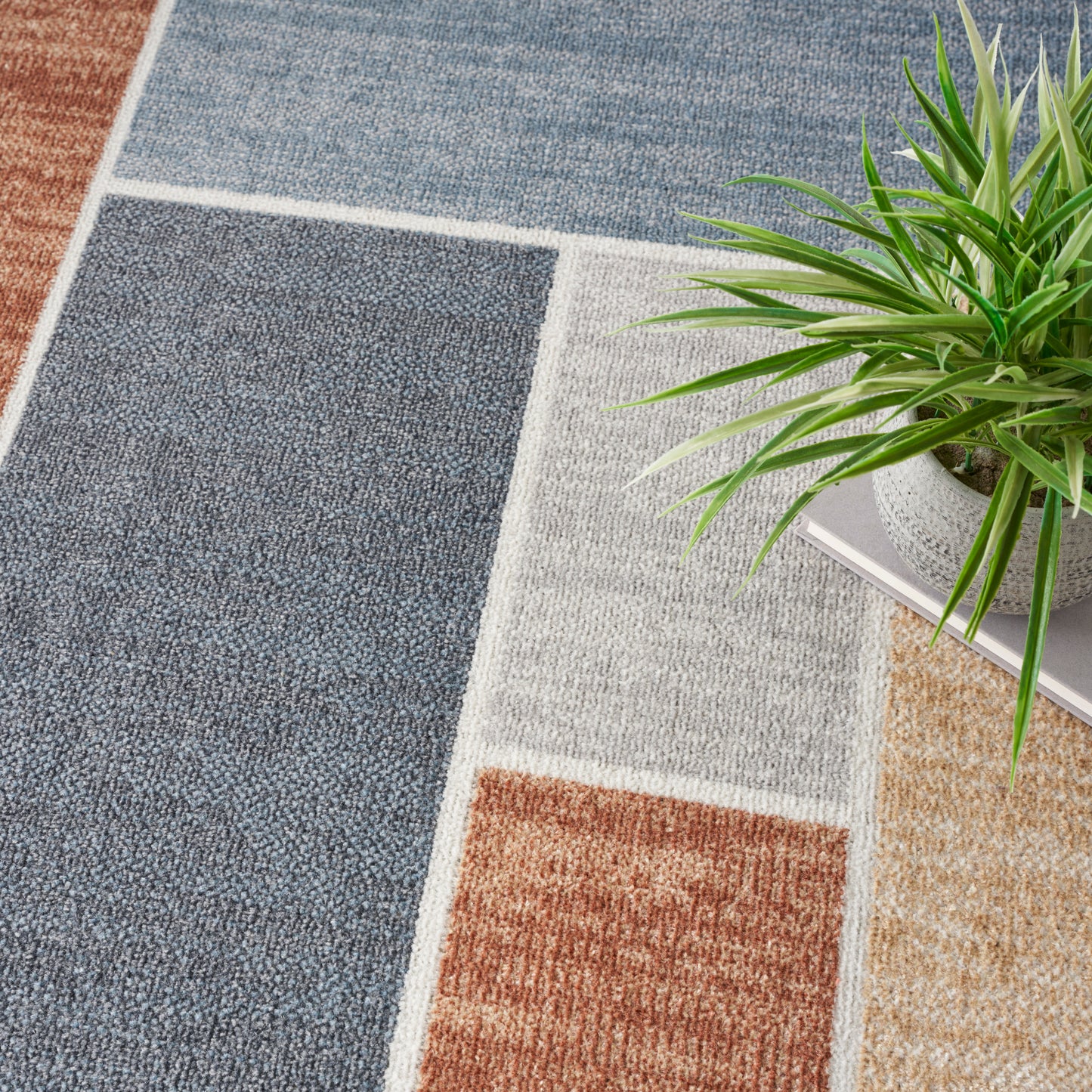 Patchwork area rug in blue, grey, beige and brown rectangles; woven texture; geometric design; green plant nearby.