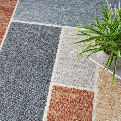 Patchwork area rug in blue, grey, beige and brown rectangles; woven texture; geometric design; green plant nearby.