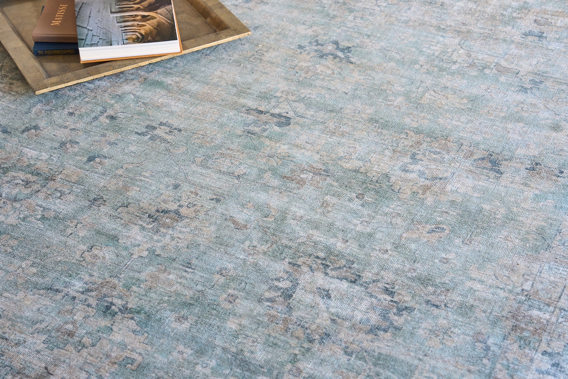 Blue-green distressed rug with faded floral pattern; wooden tray with books in top-left corner.