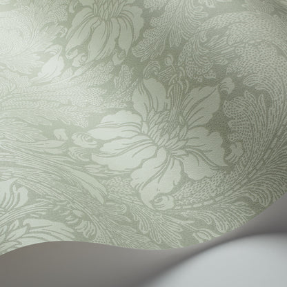Mint green damask wallpaper close-up with ornate floral scroll pattern; curved white edge peeks into corner.