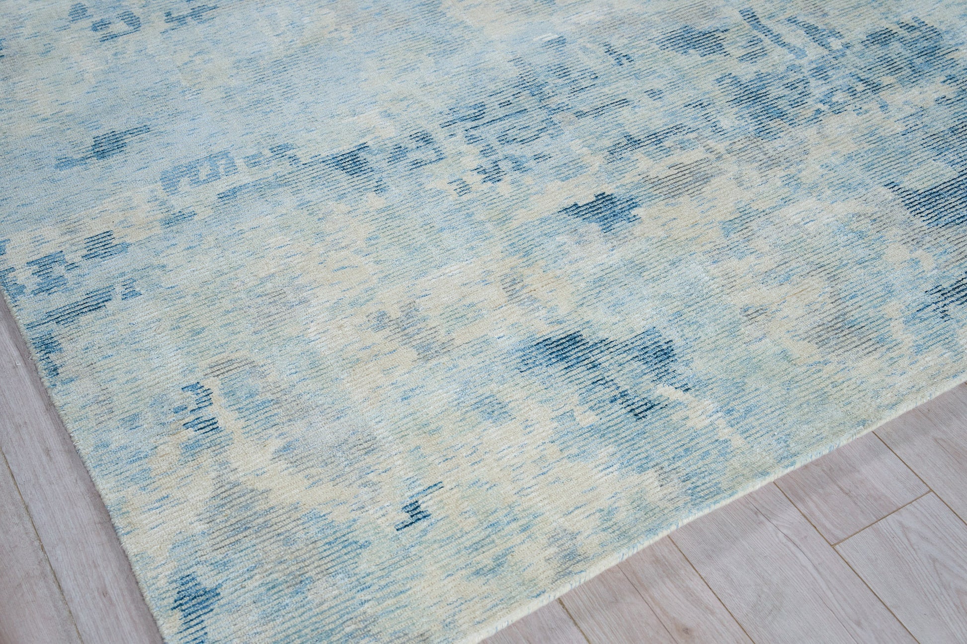 Rectangular blue & cream distressed rug with abstract geometric pattern on light wood floor