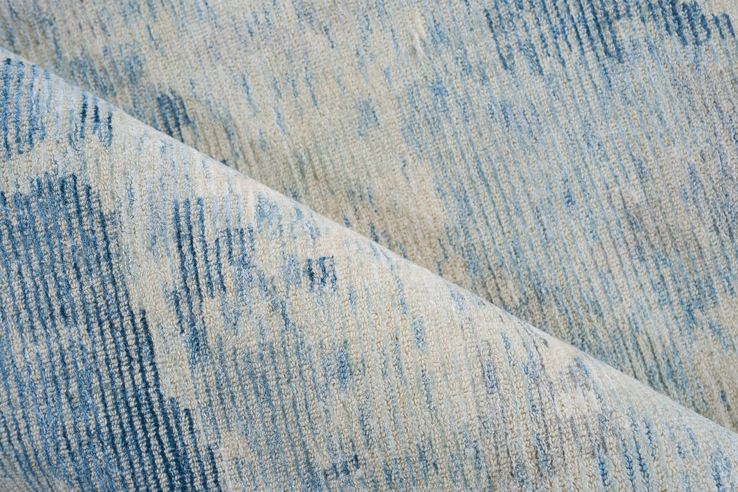 Blue and cream woven rug with textured pile and abstract vertical stripe pattern, folded corner.