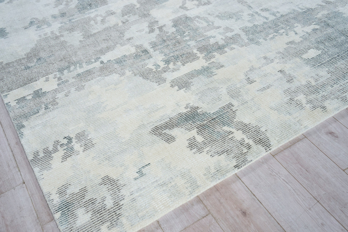 Hand loomed indoor rug in pale blue, ivory and gray with a distressed abstract pattern on light wood floor.