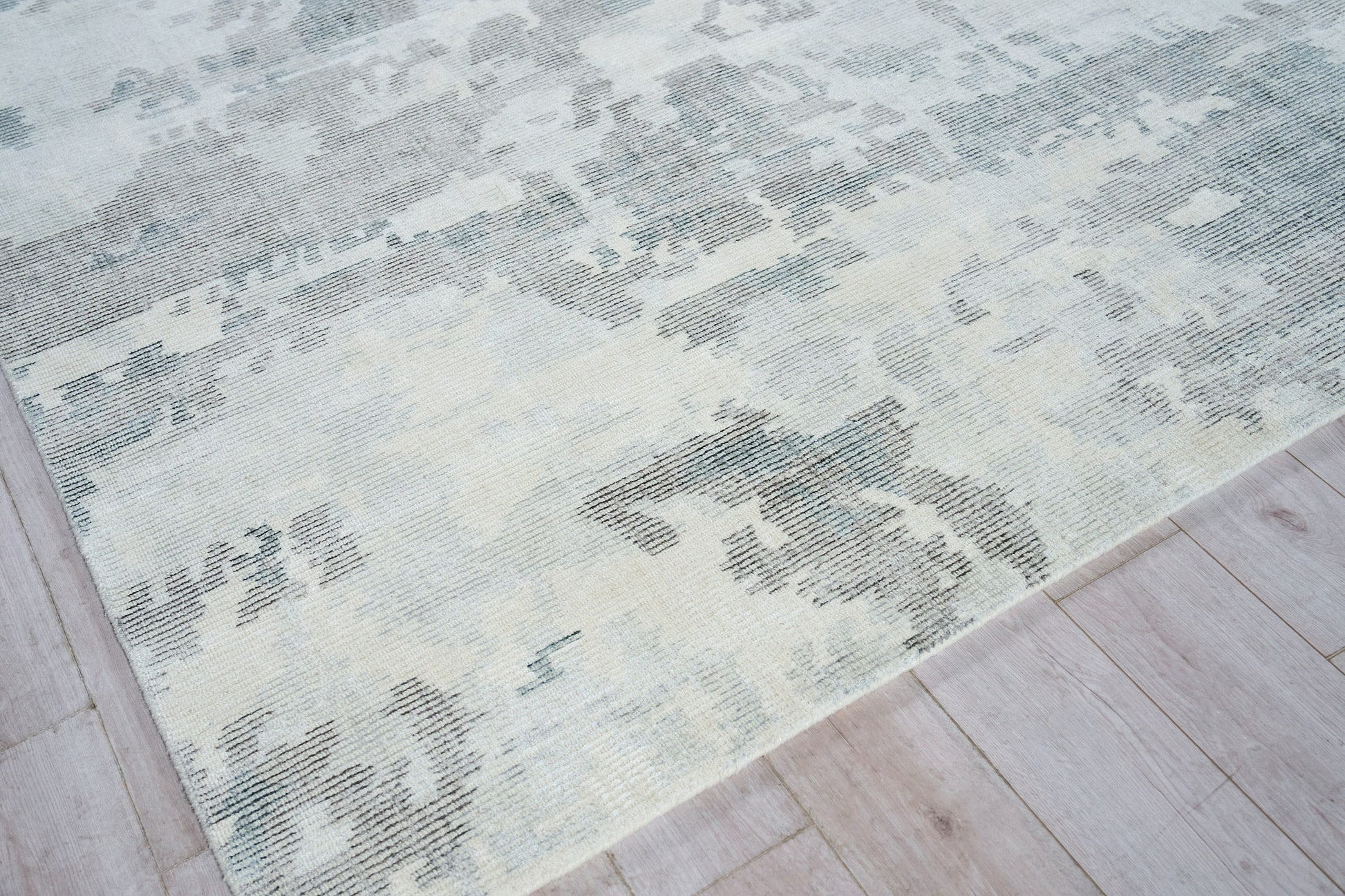 Hand loomed indoor rug in pale blue, ivory and gray with a distressed abstract pattern on light wood floor.
