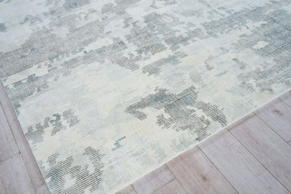 Hand loomed indoor rug in pale blue, ivory and gray with a distressed abstract pattern on light wood floor.