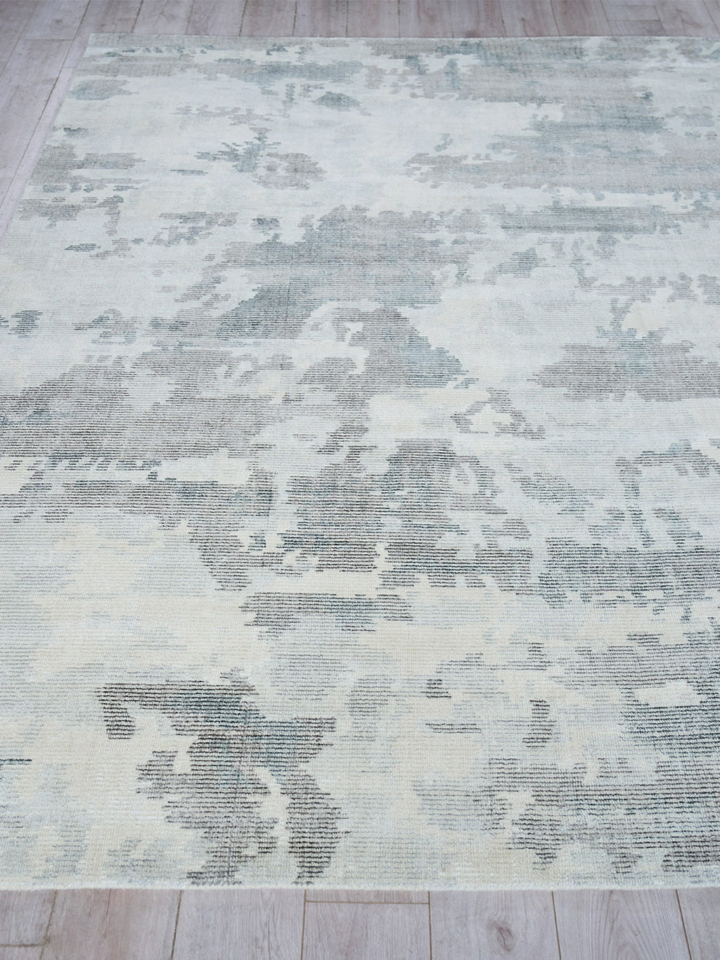 Rectangular blue-gray distressed rug with a faded abstract/floral pattern on a light wood floor.