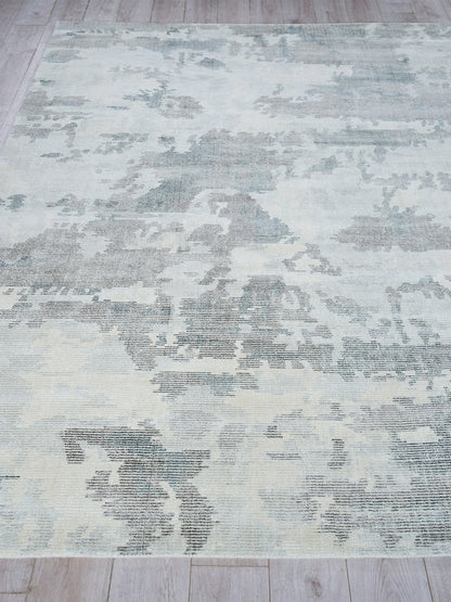 Rectangular blue-gray distressed rug with a faded abstract/floral pattern on a light wood floor.