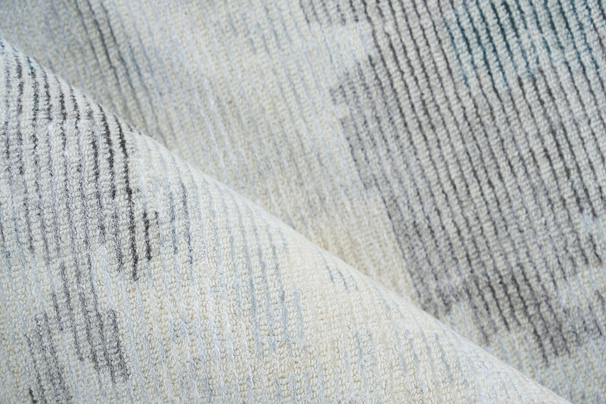 Close-up of a soft gray-blue striped woven rug with textured pile and subtle variegated threads.