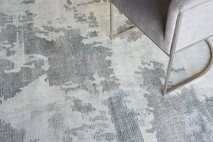 Soft textured area rug in gray-beige tones with abstract pattern; beside a gray upholstered chair with brass cantilever legs.