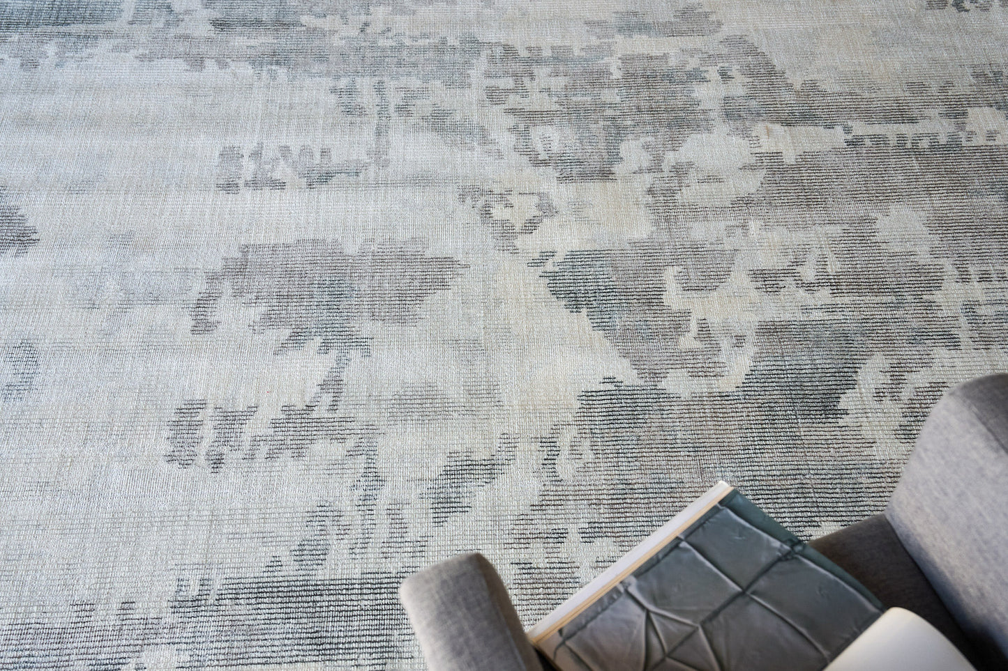 Blue-gray patterned area rug with a distressed floral motif (6' x 9'); gray sofa edge with a book.