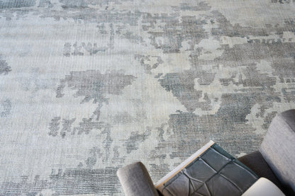 Blue-gray patterned area rug with a distressed floral motif (6' x 9'); gray sofa edge with a book.