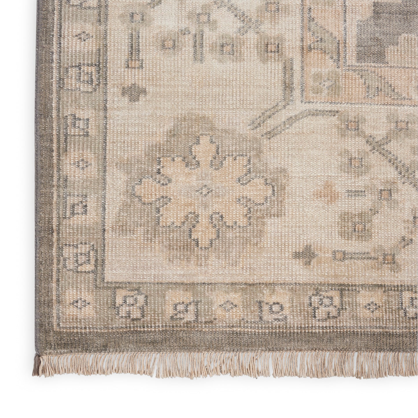 Beige woven wool oriental area rug corner with pale blue-gray floral medallion, decorative border and fringe.