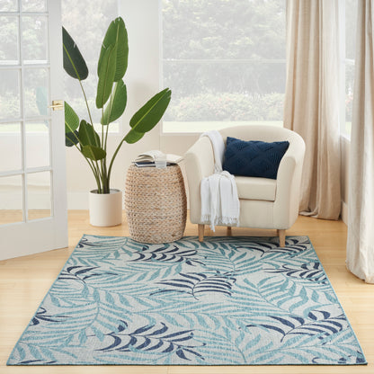 Bright living room: cream armchair, navy pillow, white throw, round woven table, tall potted plant, blue tropical rug.