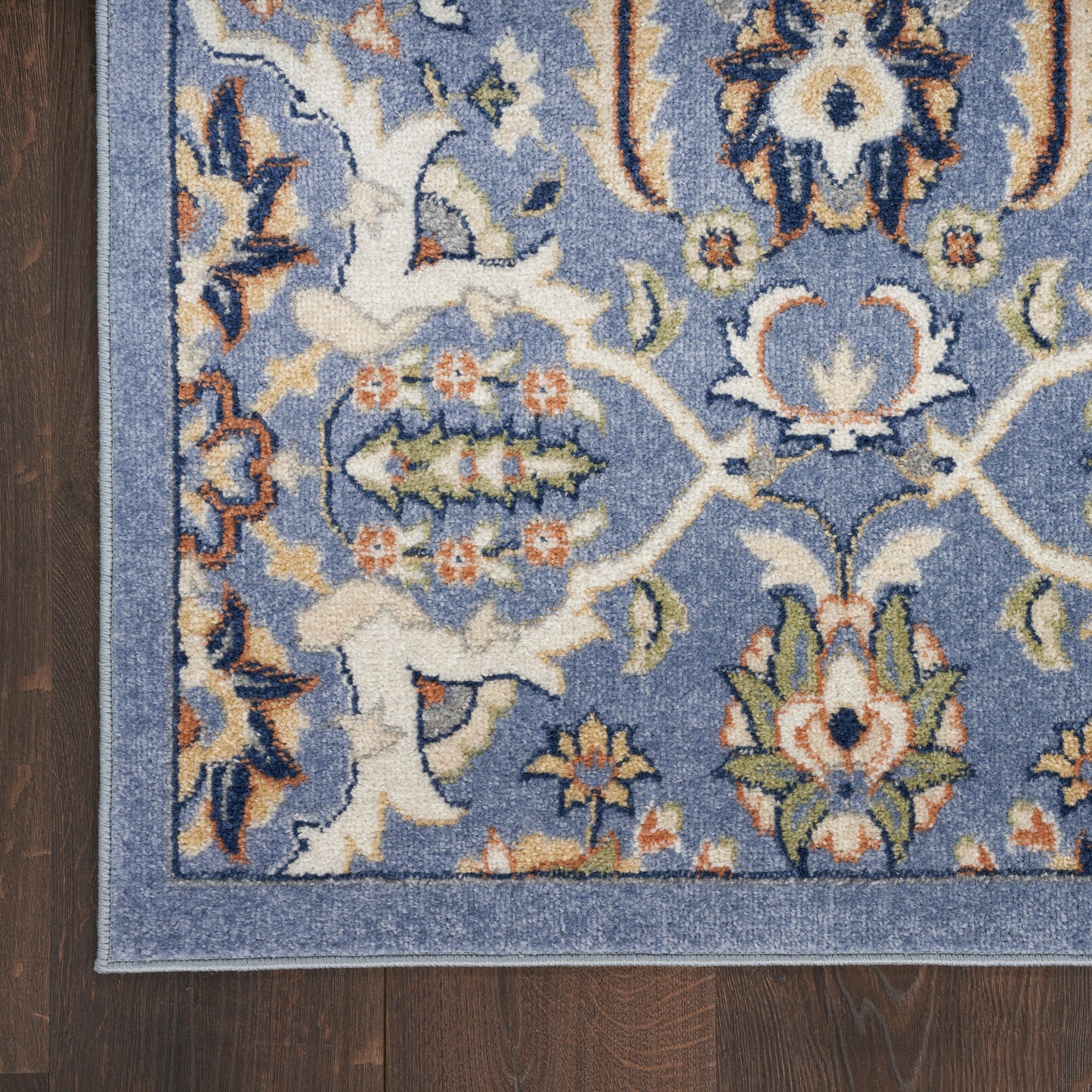 Blue oriental rug with ivory floral motifs and orange-green accents; Persian-style border on dark wood floor.