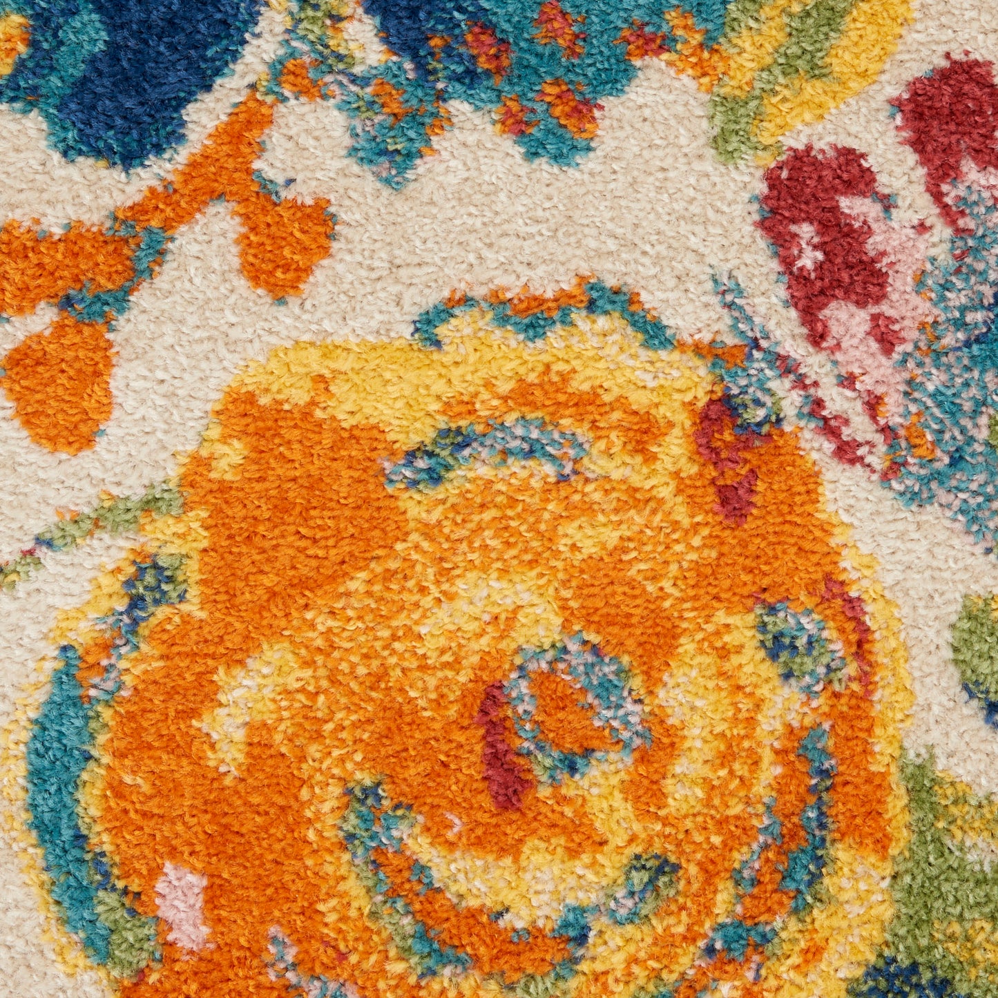 Close-up of a vibrant woven rug with an orange-yellow floral swirl on beige, accented by blue, teal, red and green.
