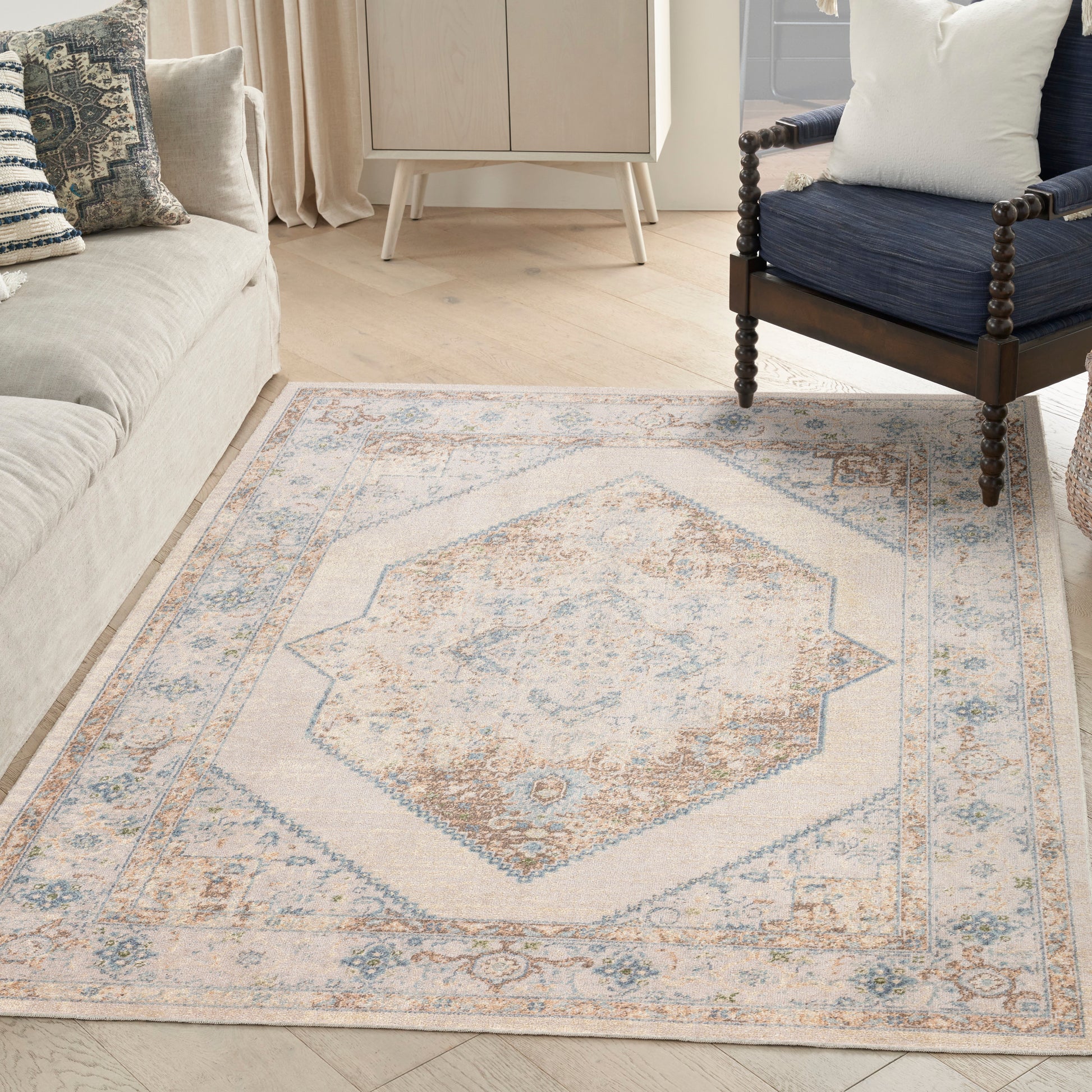 Neutral area rug with pale blue and tan geometric central medallion and ornate border, in a living room with a beige sofa.