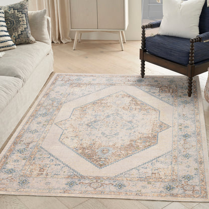 Neutral area rug with pale blue and tan geometric central medallion and ornate border, in a living room with a beige sofa.
