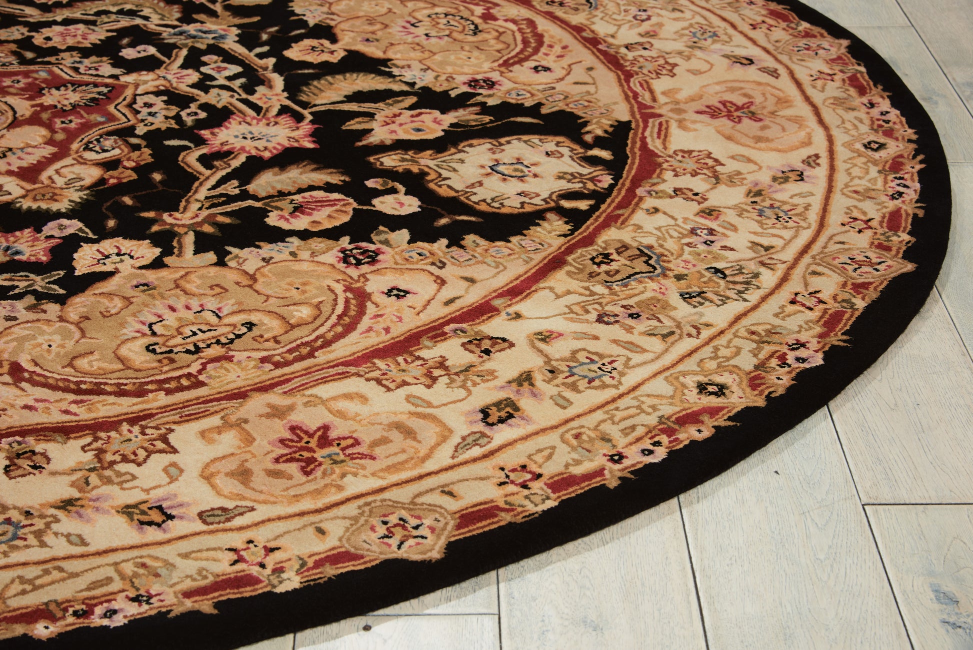 Round oriental rug with black center, ivory floral border and red accents on light tiled floor.