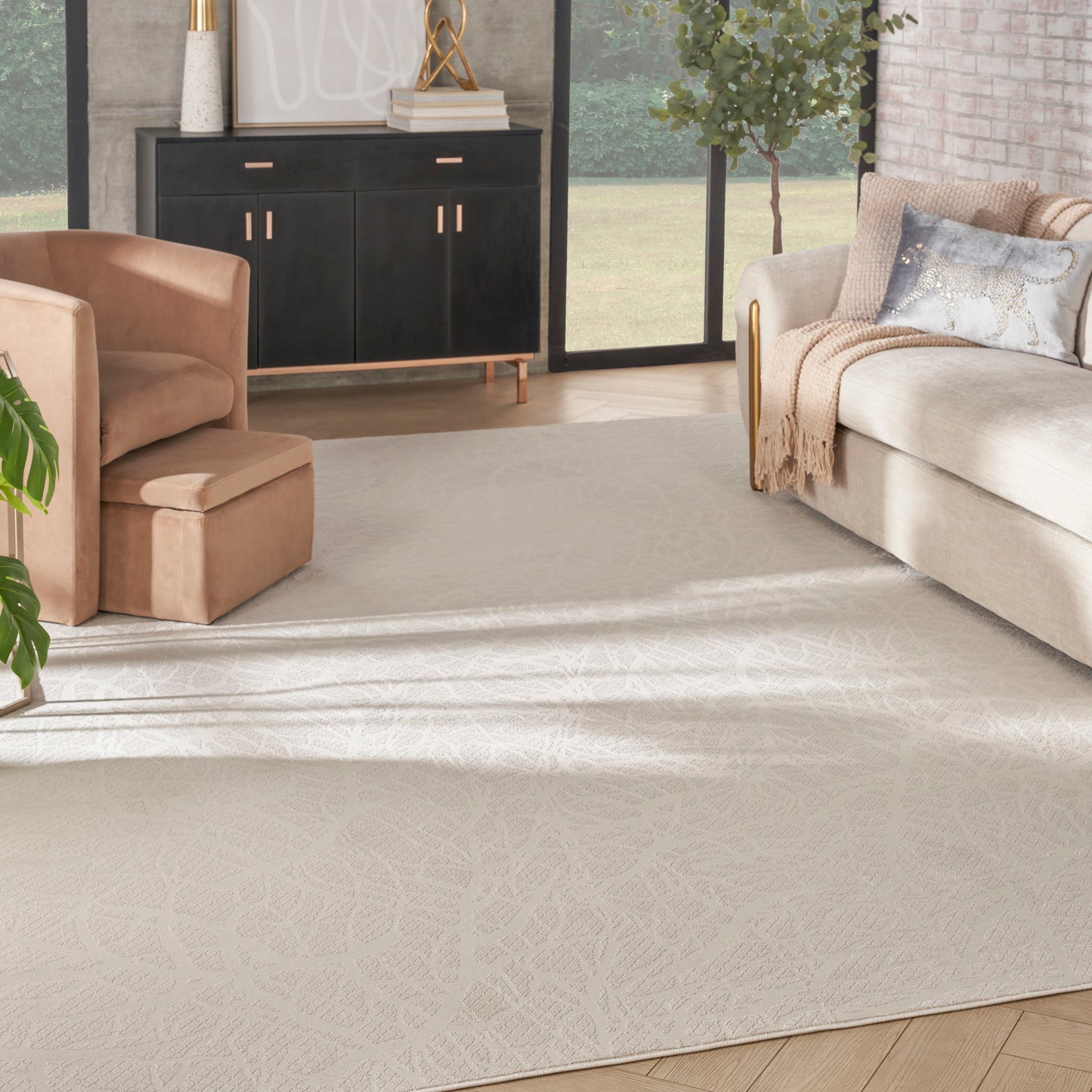 Neutral living room with large pale beige patterned rug, tan armchair, cream sofa, and black cabinet with gold handles.