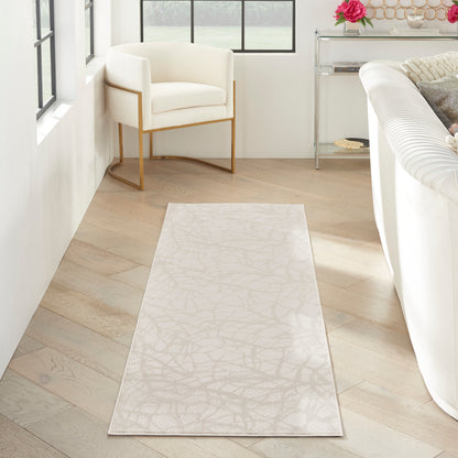 Long cream runner rug with subtle abstract leaf pattern on light wood floor beside white sofa and gold-framed chair.