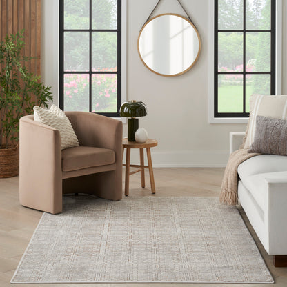 Beige curved armchair, round wood side table, black lamp, light geometric rug, white sofa, wall mirror, greenery outside.