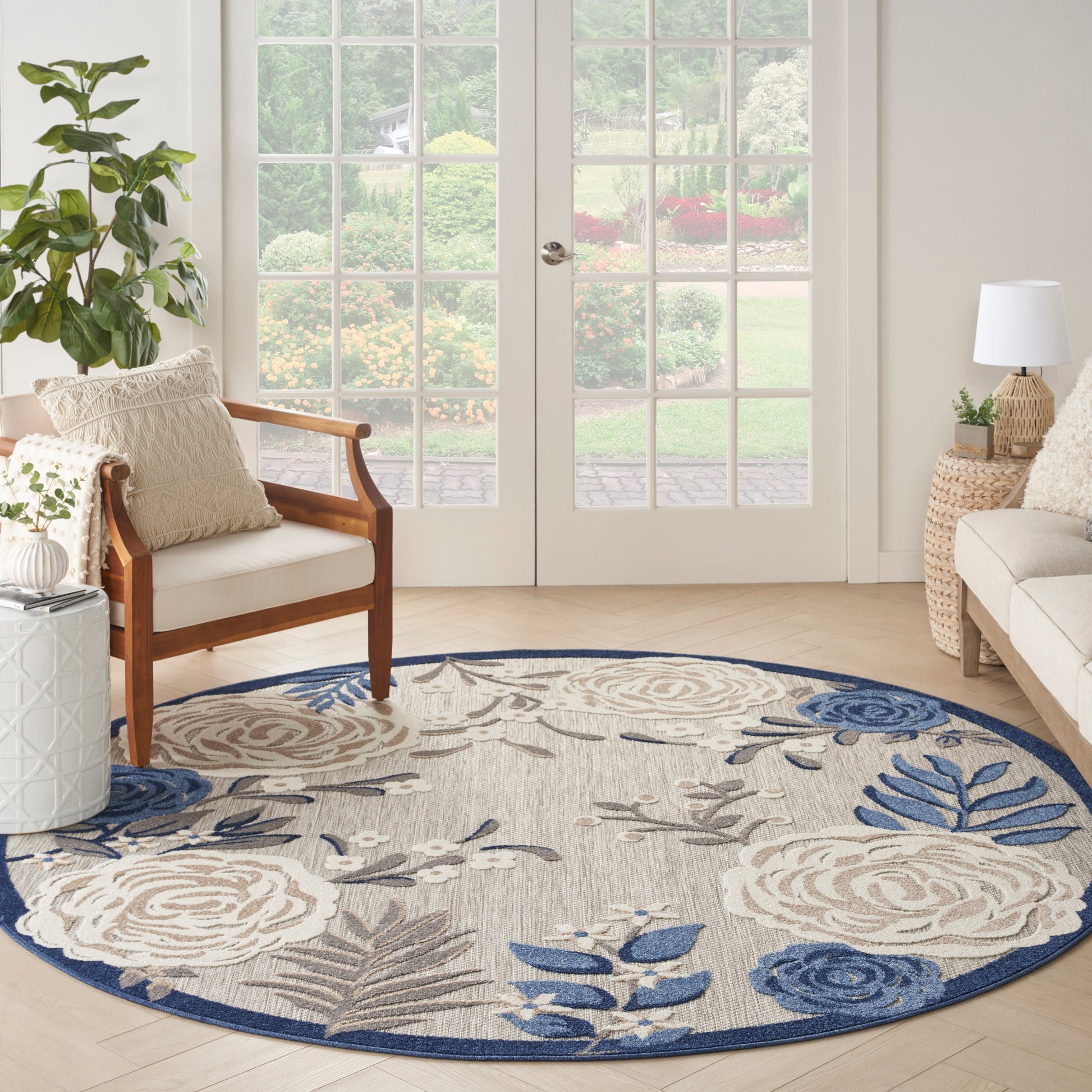 Round beige and blue floral round rug with blue border in a bright living room with wood and wicker seating, glass doors