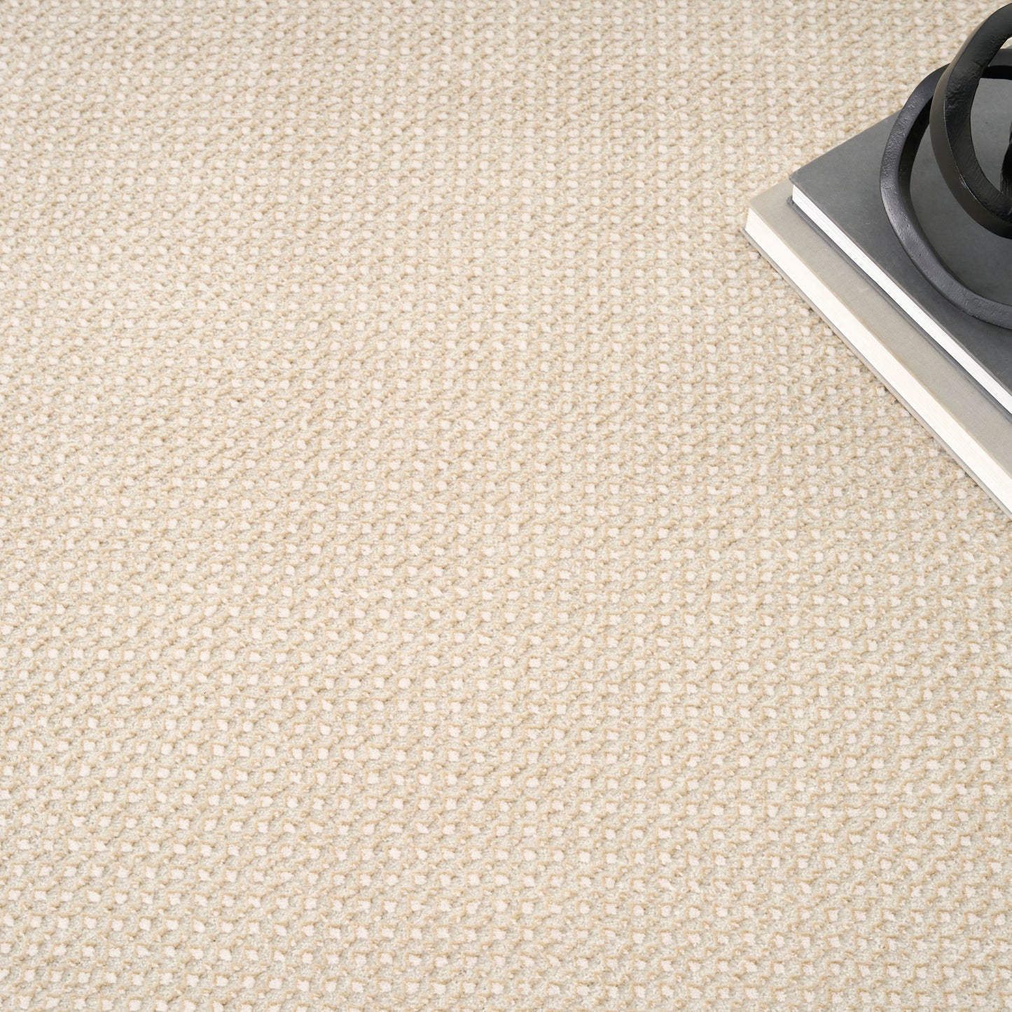 Beige woven rug with loop texture; corner shows a metal panel and black circular burner ring.