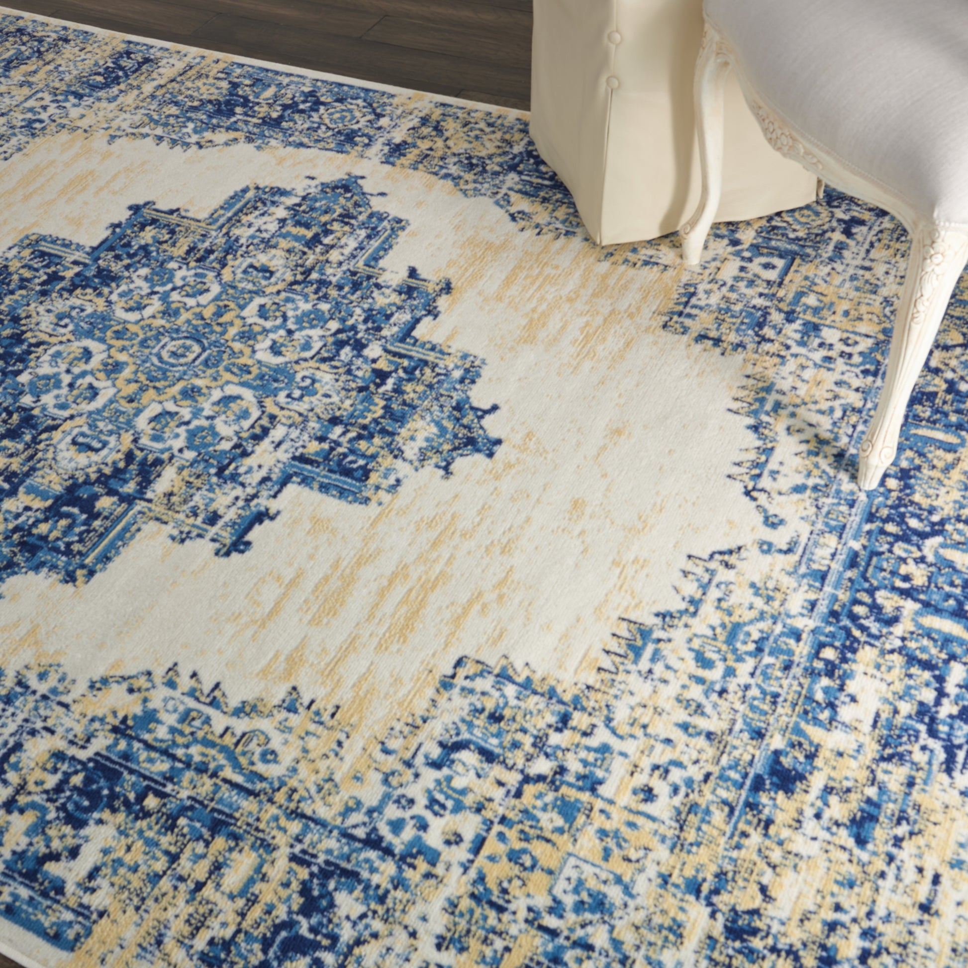 Rectangular blue-beige Persian-style area rug with an intricate medallion motif under a white ornate chair.