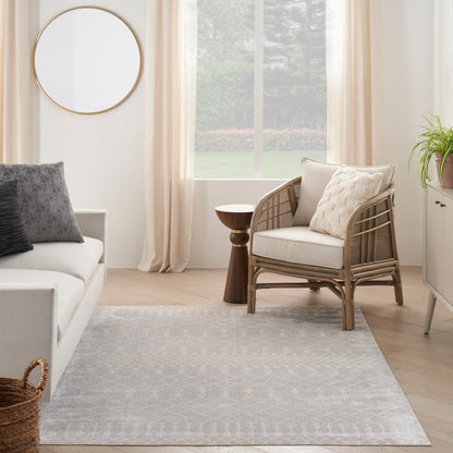 Bright living room with light wood floors, a rattan armchair with beige cushions, circular mirror, and a gray patterned rug.