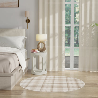 Neutral bedroom with round plaid rug, white nightstand, sculptural lamp, bed with white linens, and sheer beige curtains.
