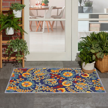Colorful floral outdoor rug on grey entry tiles, blue background with yellow and orange blooms, beside potted plants.