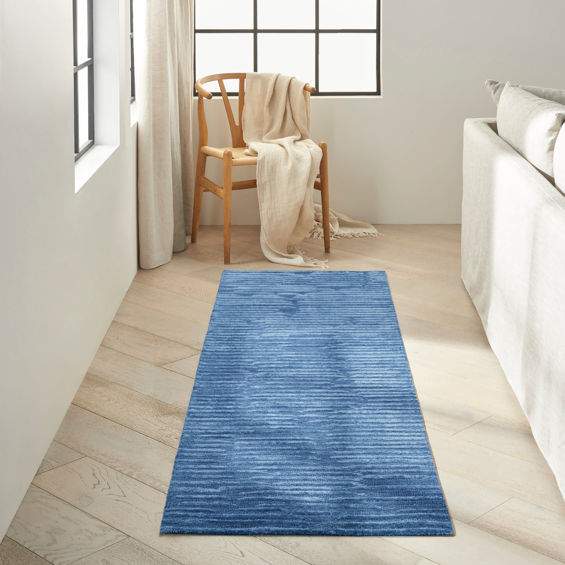 Blue textured rug runner on light wood floor beside a beige sofa and wooden chair with cream throw