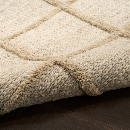 Beige woven rug with a subtle grid pattern & plush pile, folded edge visible on dark wood floor.