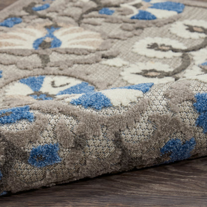 Woven area rug with taupe-gray background, blue and ivory floral medallions; dense pile and folded edge.