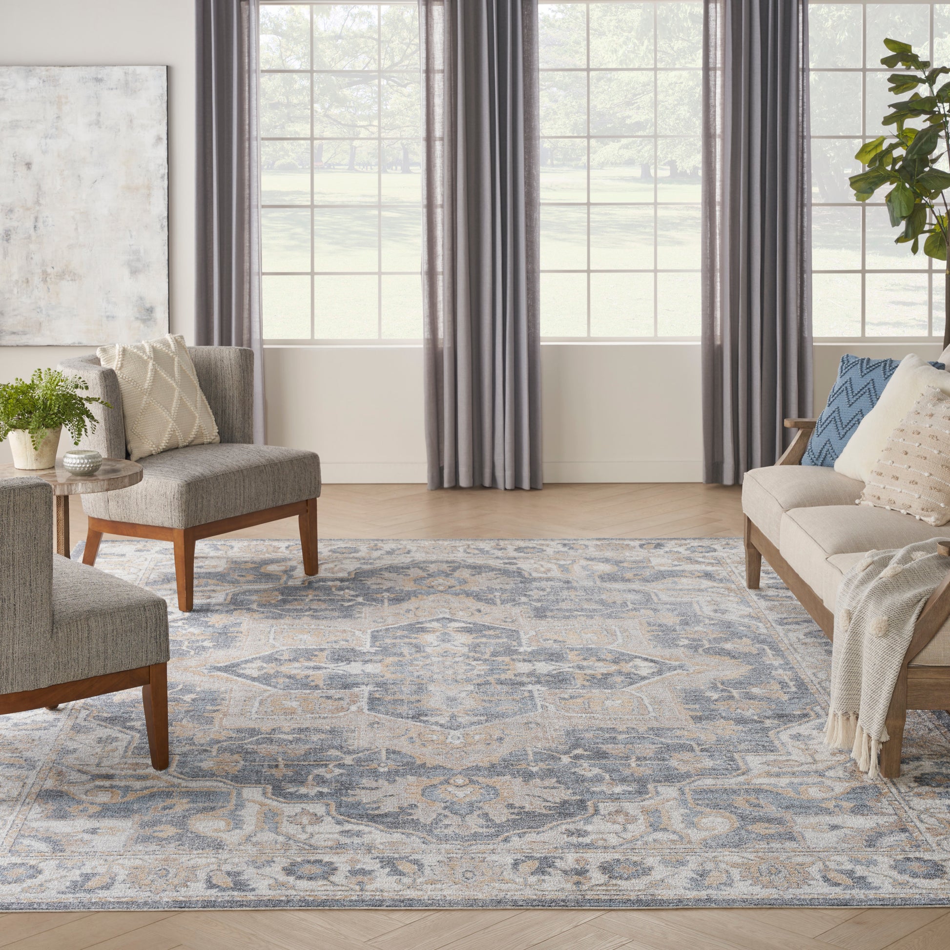 Cozy living room with blue-gray patterned rug, grey upholstered chairs, beige sofa, wooden legs, plant, and large windows.