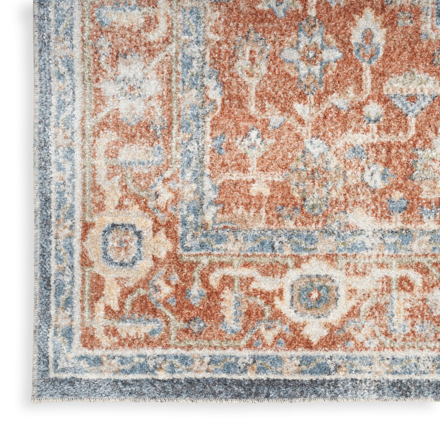 Close-up of an ornate area rug with rust-orange field, blue and cream accents and a detailed border on textured pile.